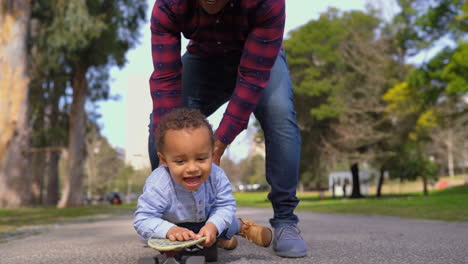 Boy-lying-on-skateboard,-rolling-to-camera-with-help-of-father